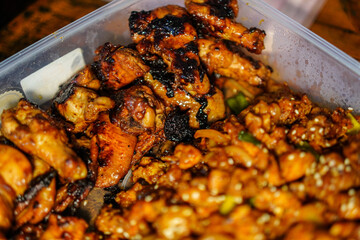 An inviting image of glazed chicken wings and tender chicken pieces, both presented in a plastic container, perfect for showcasing delicious takeout cuisine for culinary projects and dining themes.