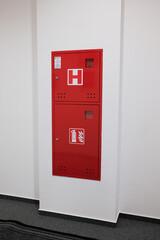 Fire hose and extinguisher cabinet attached to a white wall in a building ensuring safety and...
