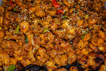 A delectable macro shot captures the rich texture and enticing colors of stir-fried chicken, garnished with sesame seeds and vibrant green onions, served and ready to enjoy the meal.
