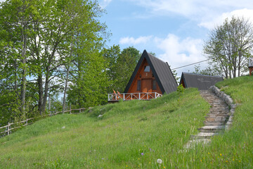A frame cabins nestled on a green hillside with stone steps and surrounding trees offer a tranquil retreat