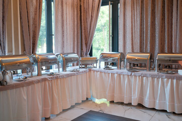 Buffet line with silver chafing dishes set up indoors with elegant backdrop curtains and marble floor for special event