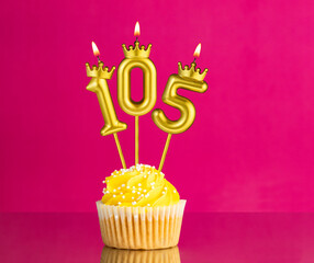 Birthday celebration with number 105 candle - Yellow cupcake on a pink background