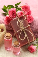 Soap bar, towels, essential oils and beautiful roses on beige table, closeup