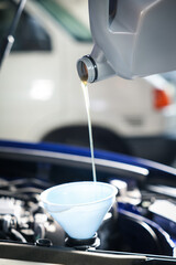 Pouring motor oil from bottle into car engine, closeup