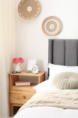 Bedside table with alarm clock, flowers and decor near bed indoors