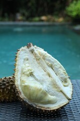 Fresh ripe durian on wicker table near swimming pool outdoors, closeup