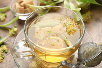 Fresh linden tea in cup, sugar cubes and flowers on wooden table, closeup