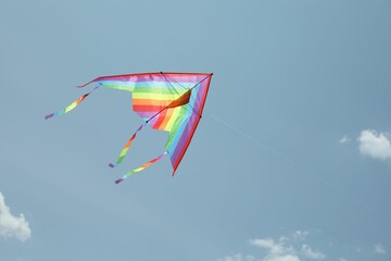 Colorful kite flying in blue sky, low angle view. Space for text
