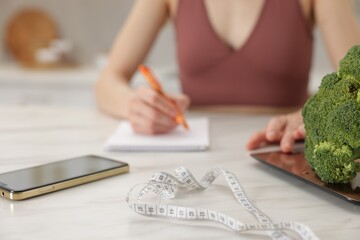 Woman developing diet plan at white marble table indoors, selective focus