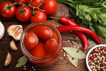 Tasty pickled tomatoes in jar and ingredients on wooden table, flat lay
