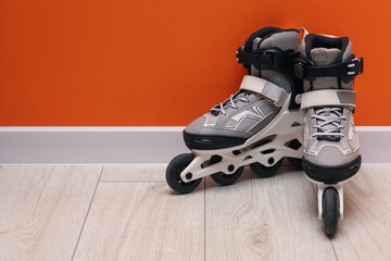 Pair of roller skates on floor near orange wall, space for text