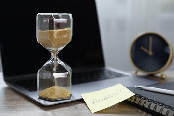 Sticky note with word Deadline, hourglass, alarm clock, stationery and laptop on wooden table...