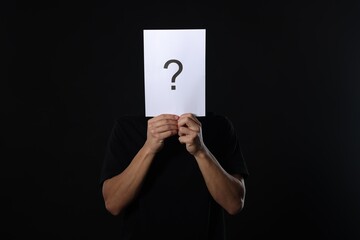 Man hiding behind paper sheet with question mark on dark background