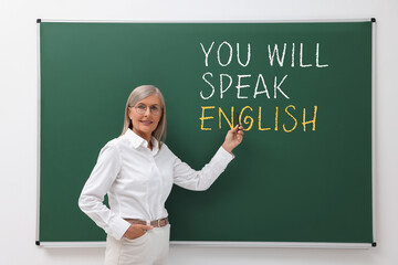 Teacher pointing at text You Will Speak English on green chalkboard. Language course