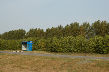 Minimalist image of a lonely rural bus stop on roadside with green trees in the background. Concept...