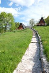 Hillside cabins offer a serene retreat amidst lush greenery Stone pathway leads to cozy dwellings under a bright sky