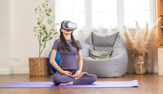 Young woman engaging in virtual reality workout session in living room, she wearing VR headset while performing yoga, modern technology with physical fitness, digital fitness trends at home - Powered by Adobe