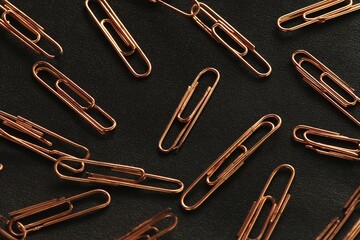 Copper paper clips scattered on a dark surface creating an organized yet chaotic arrangement