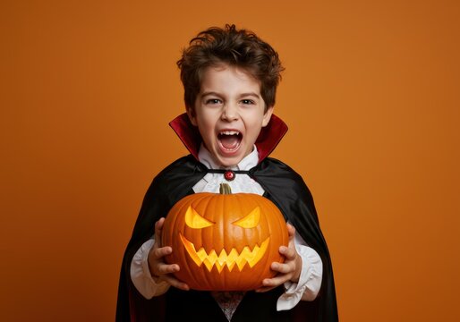 A young boy in a vampire costume holds a carved pumpkin, ready for halloween fun.