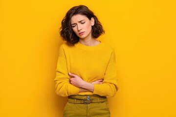 Obraz premium Image of a young woman in distress clutching her stomach due to menstrual pain set against a yellow background