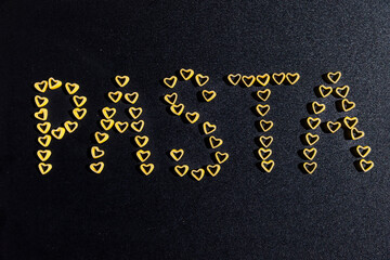 Word pasta made of raw pasta hearts on black background
