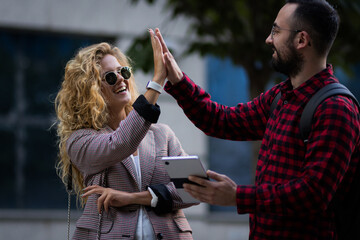 young coworkers exchanging a lively high five outdoors, celebrating success with friendly smiles...