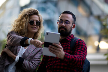 Young professionals engaging with technology on a city street while discussing ideas and sharing...