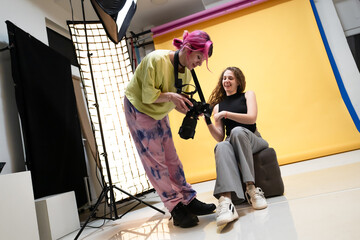 Photographer showing camera preview to model during a photoshoot in colorful studio with...