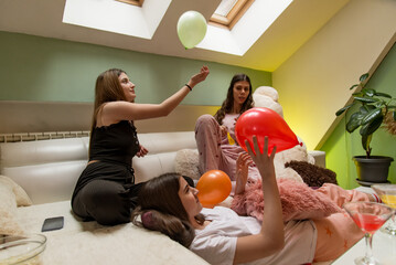 Three young women relaxing and enjoying a casual moment with balloons indoors