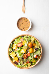 Top view of colorful vegetable salad in a rustic wooden bowl with Japanese sesame dressing on white background, Healthy, fresh, plant based eating concept