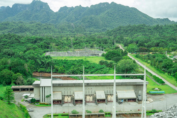 Hydropower plant building with green forest and high-voltage grid infrastructure, with mountain...