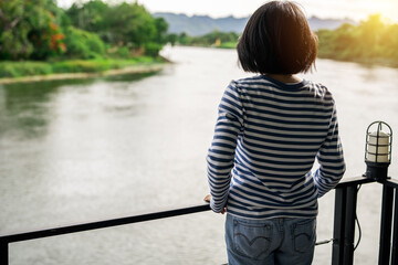 Rear view of a woman gazing at calm river. Travel retreat. Peaceful solitude, personal reflection....