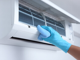 青い手袋をした手がエアコンフィルターを掃除する様子