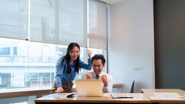 Asian adult business professionals celebrating team success achievement victory looking laptop office desk financial chart data analysis happy thrilled win together
