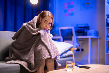 A woman is sitting on a couch wrapped in a blanket