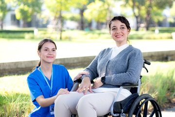 Young caucasian nurse comforting with patient while sitting on wheelchair in outdoor park, doctor...