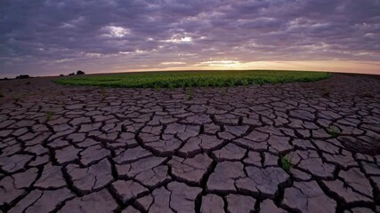Low-angle video shot of cracked, dry earth under a dramatic, cloudy sky at sunset, highlighting environmental themes and natural beauty.