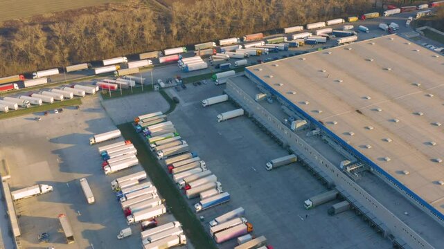 Huge logistics complex with modern warehouses and many trucks parked waiting in line along highway aerial drone view industrial transportation hub