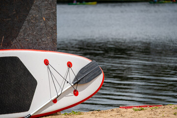 A paddleboard and paddle rest on the sand near calm water, ready for a summer adventure.