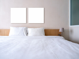 Mockup two blank square frames, 2 empty space canvas frame hanging on white wall background over wooden bed with pillows and clean blanket, decoration with lamps in hotel room background, no people.