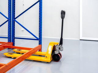 Empty yellow hand pallet truck or hydraulic pallet jack, 2.5 tons parked under rack, steel shelves,...
