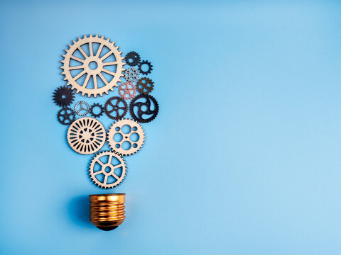 Innovation, solution workflow, creative idea, energy and power, thinking inspiration concept. Many mechanic gears and cogwheels arrange as electric light bulb on blue background with copy space.