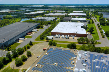Solar panels on rooftops several warehouses in lush industrial area captured on sunny day.