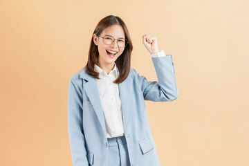 Excited Asian businesswoman raised hands celebrating success isolated against a beige background.