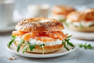 Close up of a savory bagel sandwich filled with cream cheese, fresh salmon, and arugula on a white plate, set against a light grey background