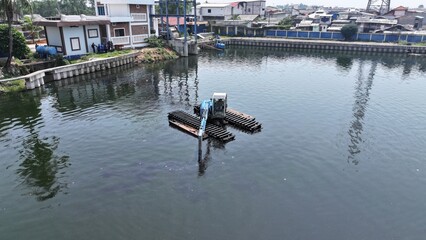 View from above of an excavator dredging a lake on the riverbank in North Jakarta