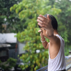 Little kid playing in summer rain in house balcony, Indian smart boy playing with rain drops during...