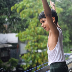 Little kid playing in summer rain in house balcony, Indian smart boy playing with rain drops during...
