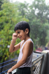 Little kid playing in summer rain in house balcony, Indian smart boy playing with rain drops during monsoon rainy season, kid playing in rain