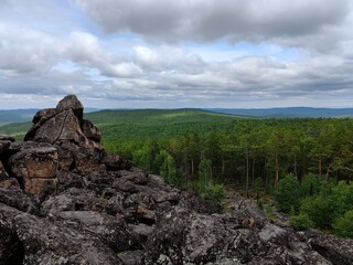 an expansive view reveals rocky summit surrounded by dense green forest and rolling hills, with...